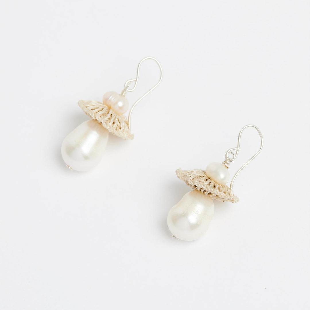 Side view of silver pearl drop earrings with woven natural fibre disc