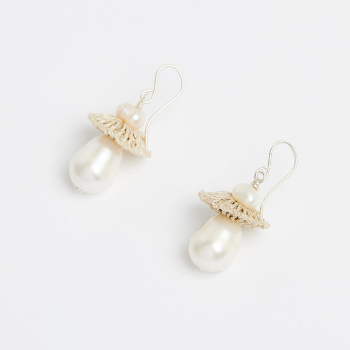 Side view of silver pearl drop earrings with woven natural fibre disc