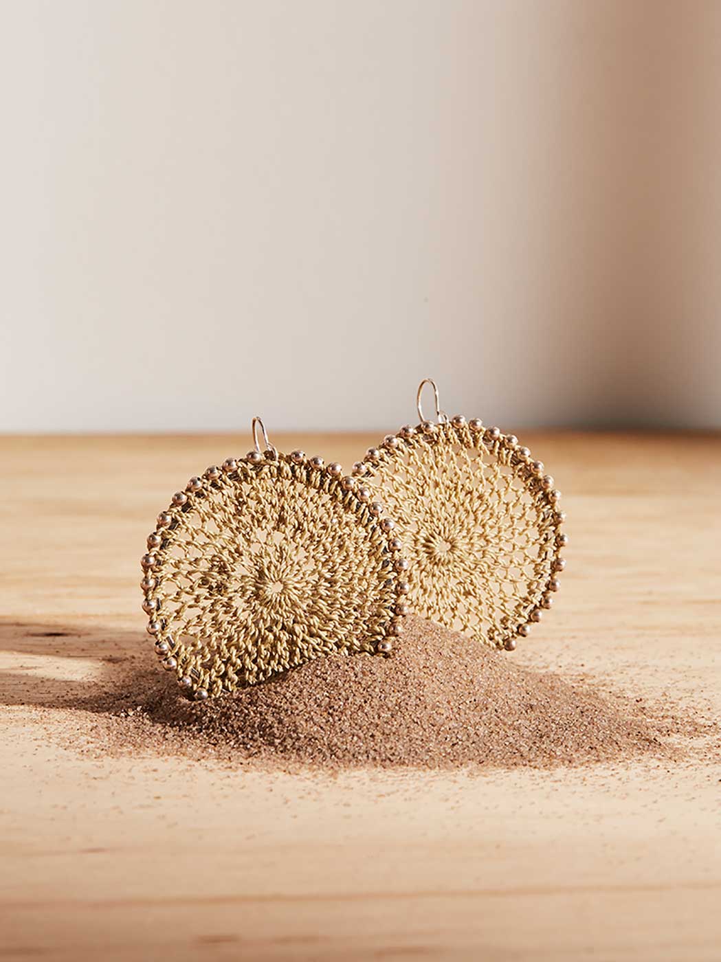Bilum and Bilas Sunset earrings with silver beading on natural fibre woven discs in sand still life.